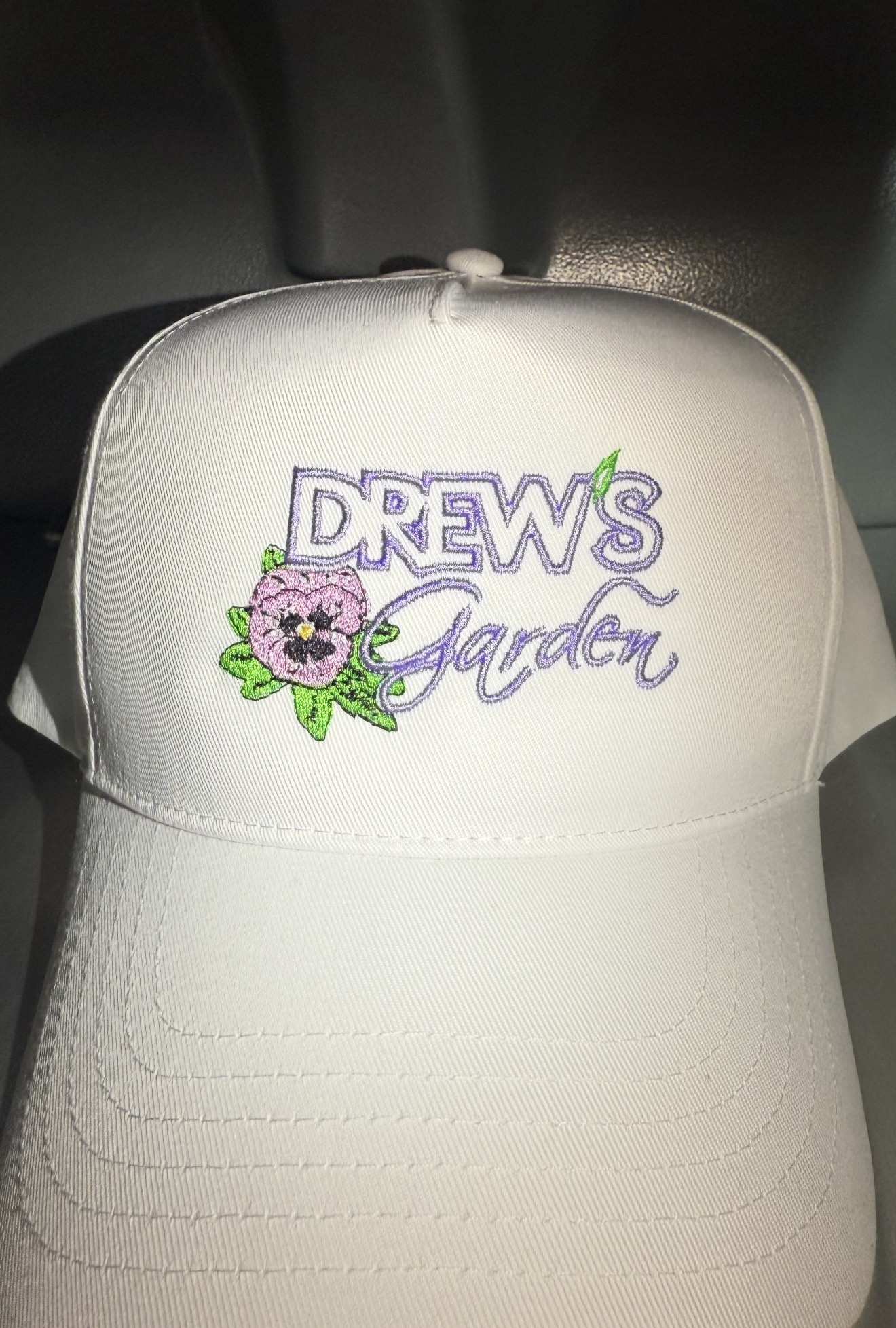 White cap with purple Drew's Garden lettering and colorful floral embroidery