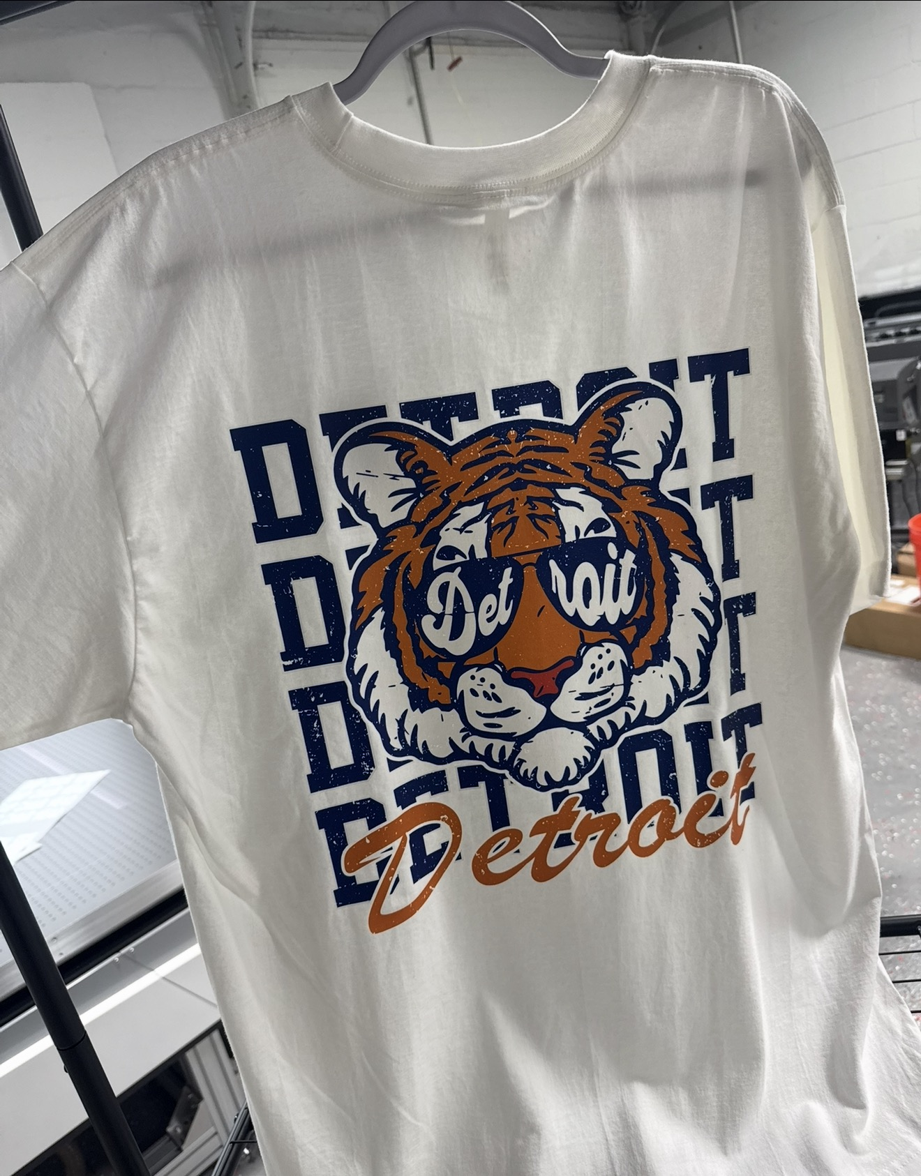 White T-shirt with a navy and orange Detroit tiger graphic wearing sunglasses