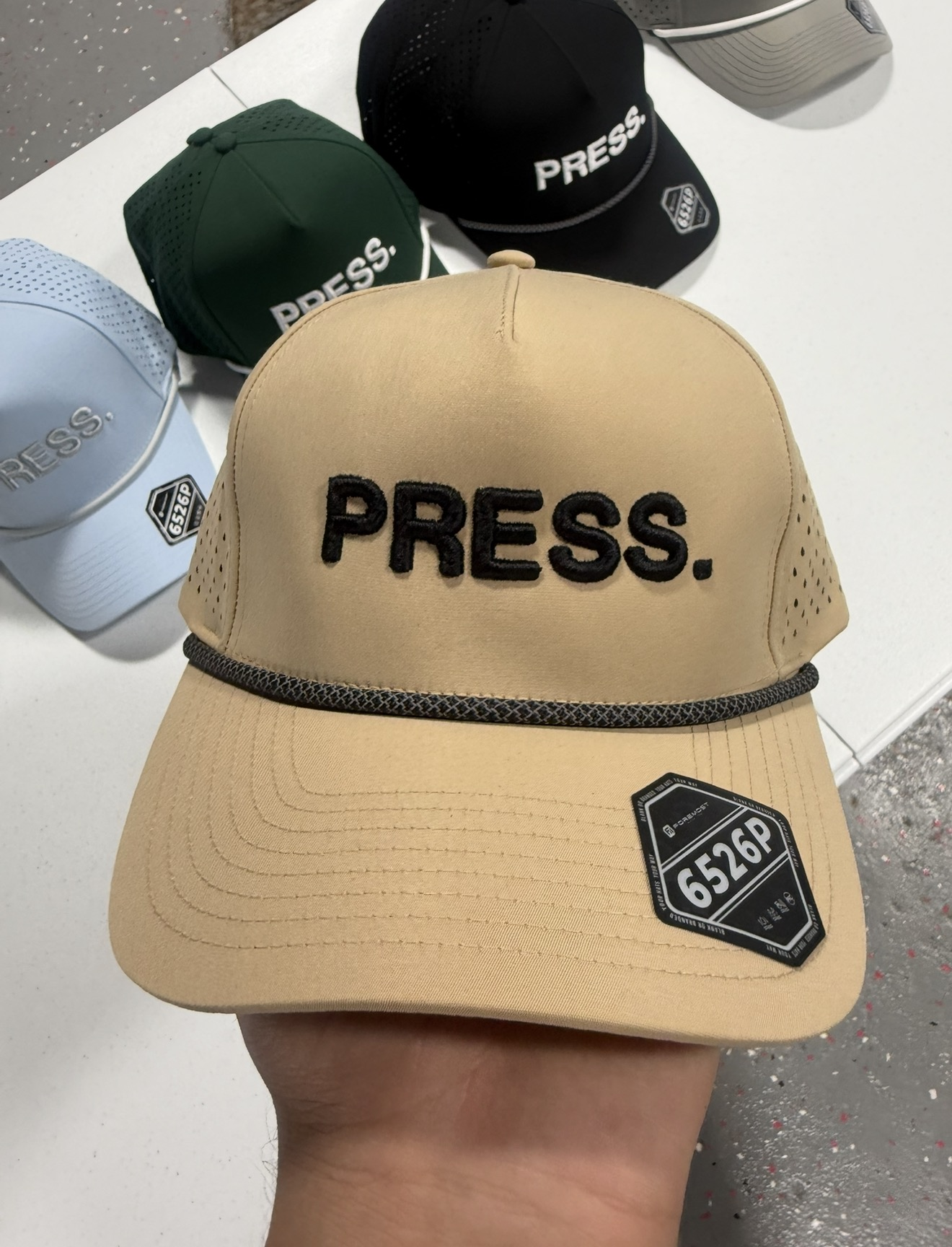 Tan cap with black PRESS. embroidery alongside green, black and blue caps