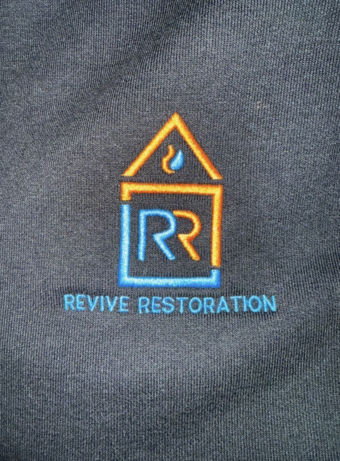 Blue and orange Revive Restoration logo embroidered on dark fabric